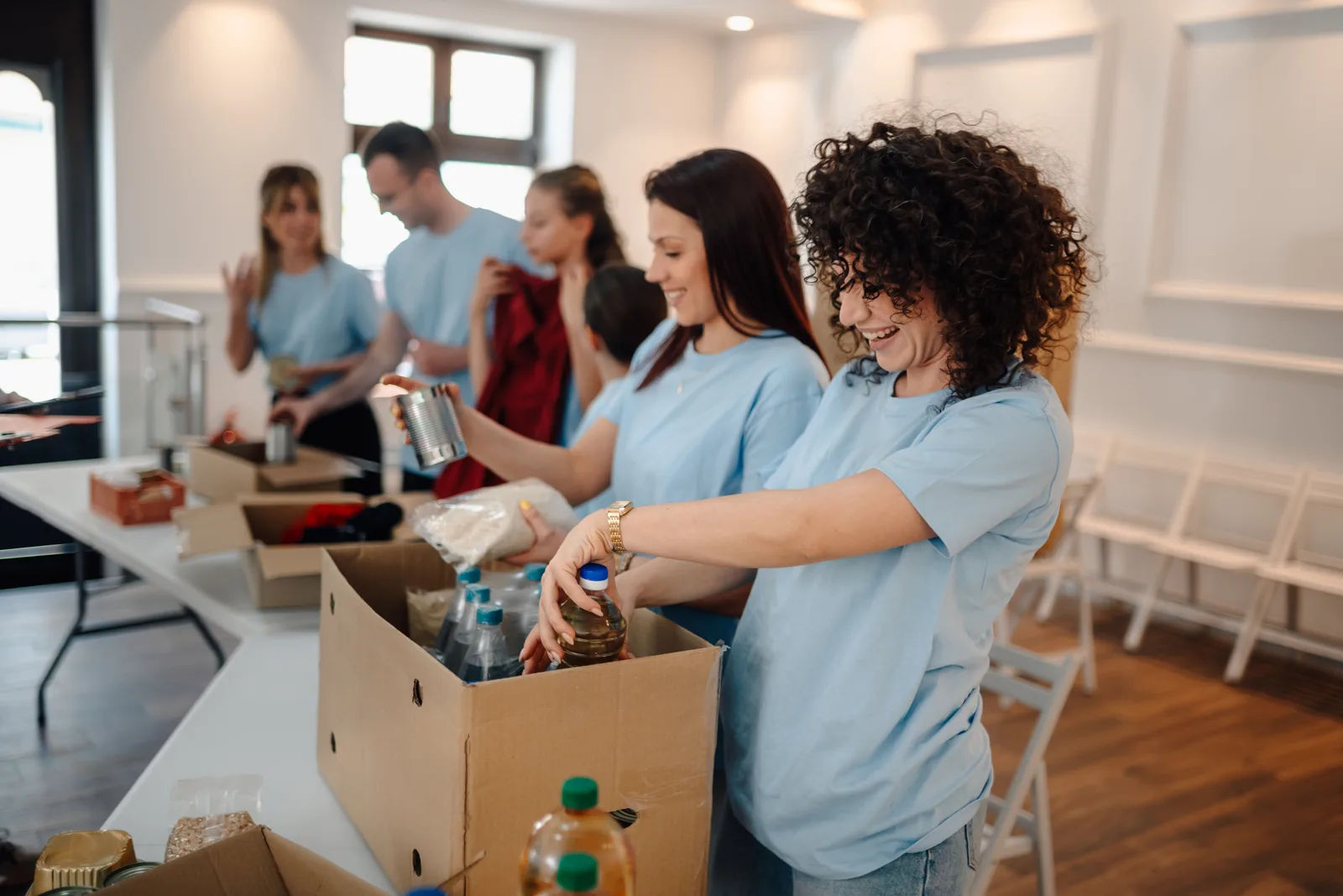 Volunteers in blue T-shirts smile as they pack food donations into boxes