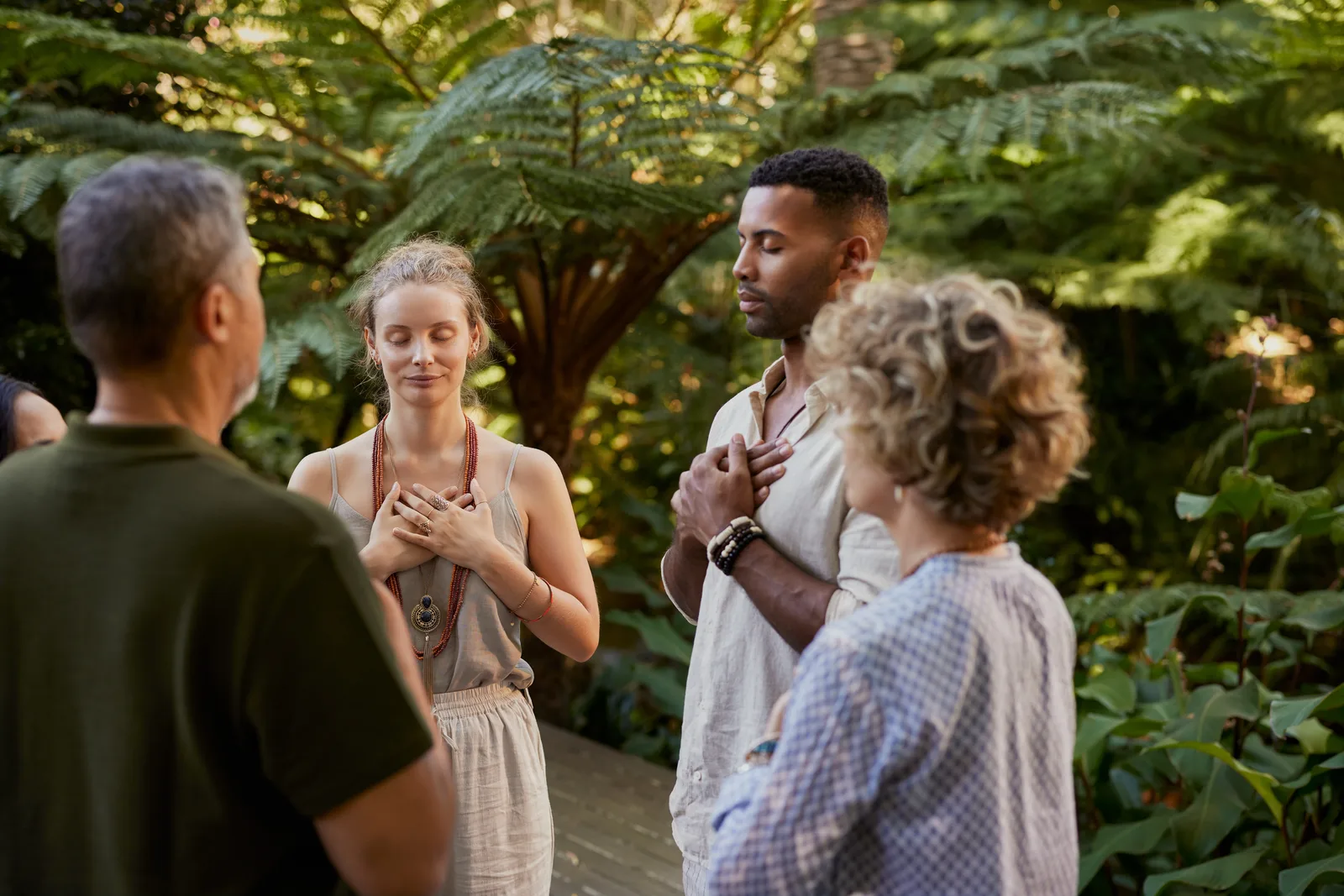 Four adults stand together in a lush garden, eyes closed, hands over their hearts